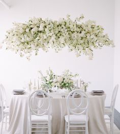 the table is set with white linens and flowers hanging from the ceiling above it