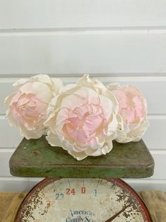 three pink flowers sitting on top of an old clock