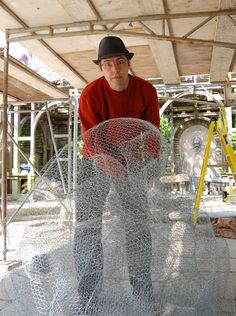 a man in red shirt and black hat standing next to a wire sculpture