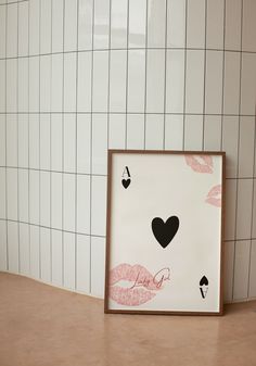 a white tiled wall next to a wooden frame with pink and black lipstick prints on it