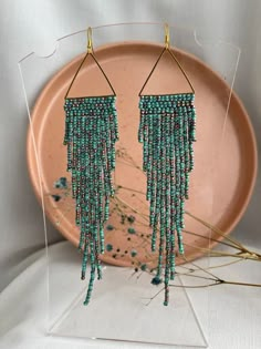 a pair of blue beaded earrings on a pink plate next to some dried flowers