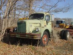 an old green truck parked in a field next to some trees and other junk cars