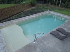 an empty swimming pool with lounge chairs next to it and a wooden fence in the background