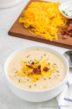 a bowl of soup with cheese and bacon on the side next to a cutting board