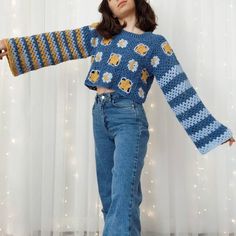 a woman in jeans and a knitted sweater is posing for the camera with her arms outstretched