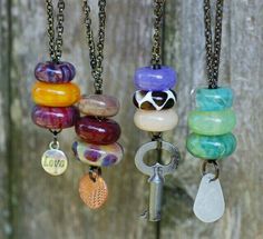 four different necklaces hanging from chains on a wooden fence