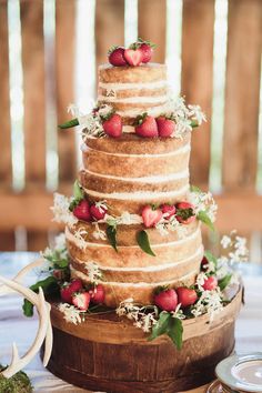 a three tiered cake with strawberries and flowers on the top is surrounded by antlers