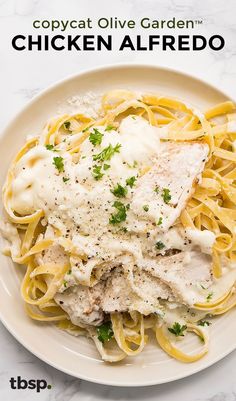 a white plate topped with chicken alfredo next to a fork and knife on a marble table