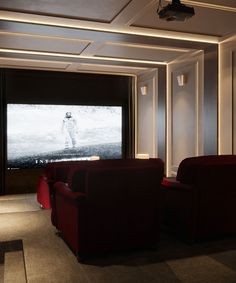 an empty room with two red chairs and a large screen in the corner that is lit up