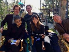 three men and two women posing for a photo in the woods with one woman sitting on a chair