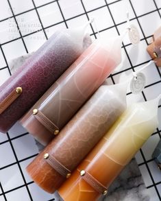 four different colored candles sitting on top of a tiled counter next to each other,