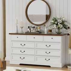 a white dresser topped with lots of drawers and a round mirror on top of it