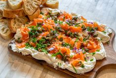 a wooden cutting board topped with lots of food next to bread slices and salad dressing