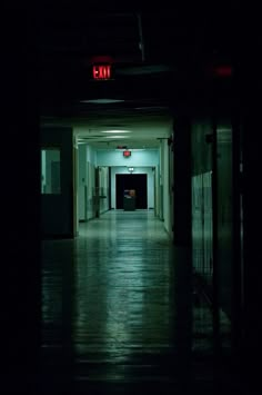 an empty hallway in the dark with a red sign on it's left side