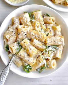 two white bowls filled with pasta and spinach on top of a table next to silverware