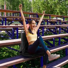 a woman sitting on top of a wooden bench in front of blue metal railings