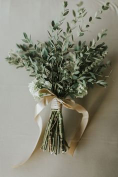 a bouquet of greenery tied to a white wall with a ribbon around it on a table