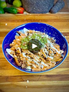 a blue plate topped with pasta covered in sauce and toppings on top of a wooden table