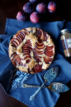 a pie sitting on top of a blue napkin next to some plums and a bottle