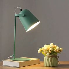 a green lamp sitting on top of a wooden table next to a vase with flowers