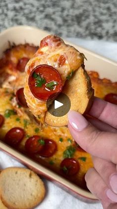 a person is taking a piece of pizza from a casserole dish with tomatoes and cheese