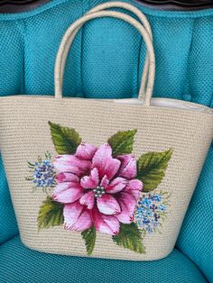 a pink flower painted on the side of a white purse sitting on top of a blue chair