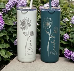 two insulated tumblers sitting next to each other in front of some purple flowers