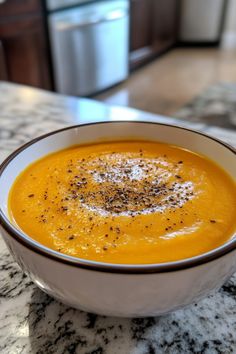 A bowl of creamy orange soup topped with black pepper on a marble countertop. Soup Lovers