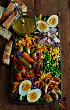 an assortment of vegetables and meats on a platter with eggs, peas, carrots, bread