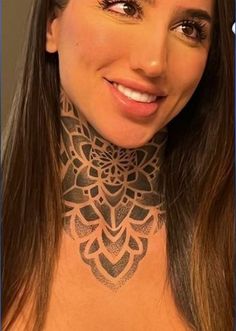 a woman wearing a neck tattoo with an intricate design on her chest, smiling at the camera