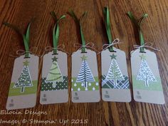 four tags with christmas trees on them sitting on a wooden table next to green ribbon