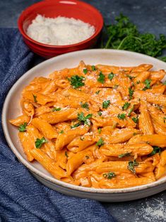 a white bowl filled with pasta and parsley next to a red bowl full of rice