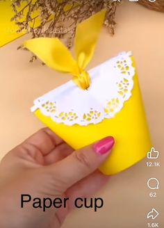 a hand holding a paper cup with a yellow bow on it's top and the words paper cup below