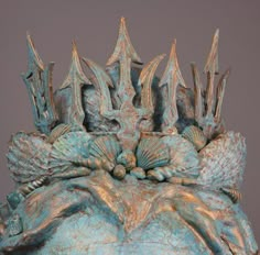 a blue sculpture with many different designs on it's face and hands, sitting in front of a gray background