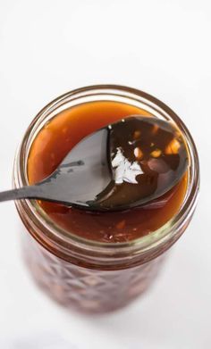 a spoon full of caramel sauce on a white surface with the lid partially open