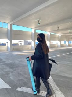 a woman wearing a mask and carrying a large blue tube in an empty parking lot