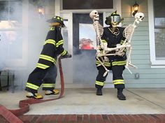 two firemen in skeleton costumes standing on the front porch with their hoses out