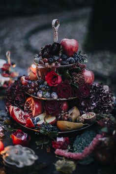 a three tiered tray filled with fruit and flowers on top of a table next to candles