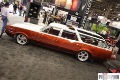 an orange and white station wagon on display at a car show with people standing around