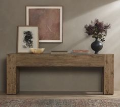 a wooden table with two vases on top of it next to pictures and a rug