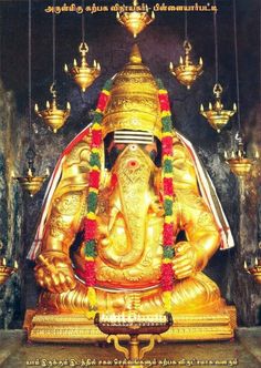 a golden statue sitting inside of a building next to hanging lights and candles in front of it