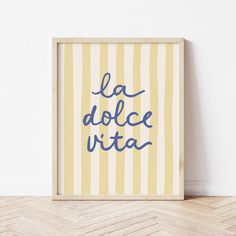 a framed poster with the words la dolce vita in blue ink on a yellow striped background