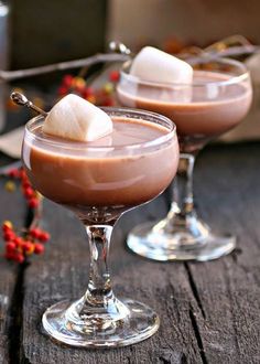 two glasses filled with drinks sitting on top of a wooden table