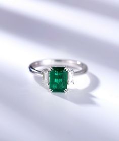 an emerald and diamond ring sitting on top of a white surface with the light shining through it