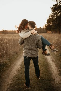 a man carrying a woman on his back while walking down a dirt road in the middle of a field