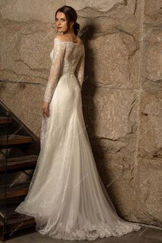 a woman standing in front of a stone wall wearing an off the shoulder wedding dress