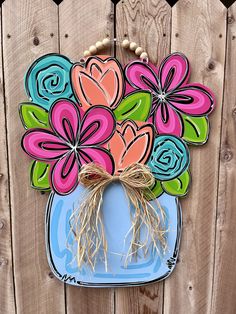 a blue vase with flowers painted on it hanging from a wooden fence next to a wall