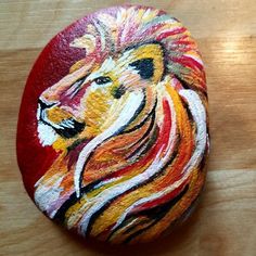 a painted rock with a lion on it's face and the colors red, yellow, orange, and white