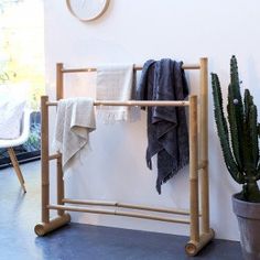 a bamboo rack with towels and blankets on it next to a potted cacti