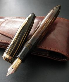 a pen sitting on top of a brown leather case next to a black and gold pen